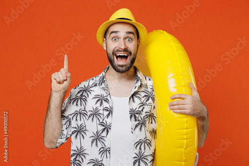 Young tourist man wear beach shirt hat hold inflatable ring holding index finger up with great new idea isolated on plain orange background studio portrait. Summer vacation sea rest sun tan concept.