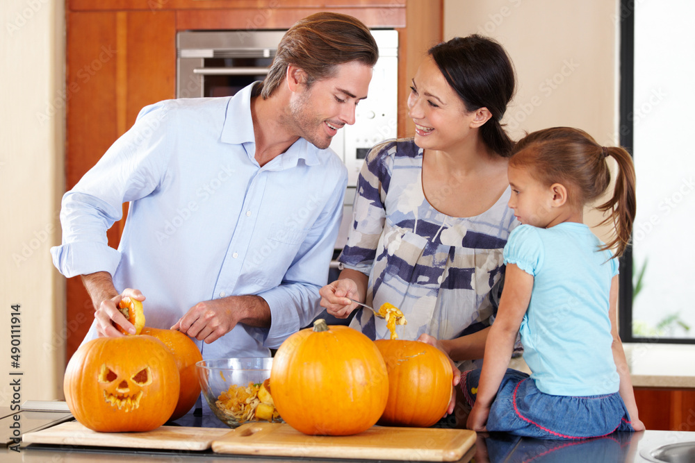 Prepping the pumpkin for Halloween. A young mother and father standing with their young daughter in a kitchen preparing Jack Olanterns for Halloween.