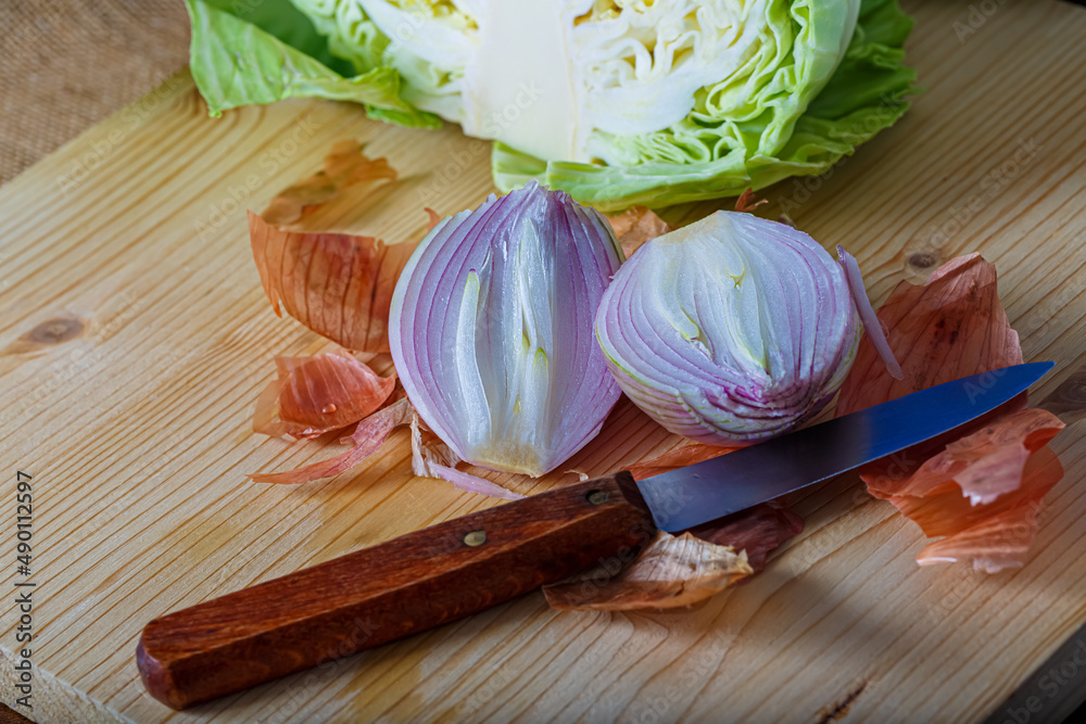 Top view of raw vegetables cut into two parts. Purple onion with peel and white cabbage on a wooden board, a small knife.
