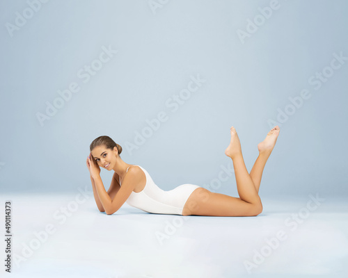 A young, slim and healthy woman in a white swimsuit poses in the studio. Girl with perfect skin. Body care, rejuvenation, sport and diet.