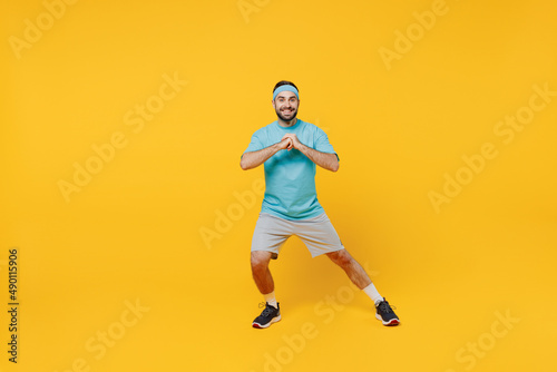 Full body fun young fitness trainer instructor sporty man sportsman in headband blue t-shirt spend weekend in home gym do lunges isolated on plain yellow background. Workout sport motivation concept. © ViDi Studio
