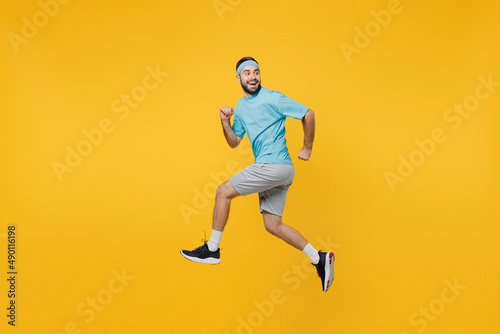 Fototapeta Naklejka Na Ścianę i Meble -  Full size side view strong young fitness trainer instructor sporty man sportsman wear headband blue t-shirt jump high run fast look aside isolated on plain yellow background. Workout sport concept