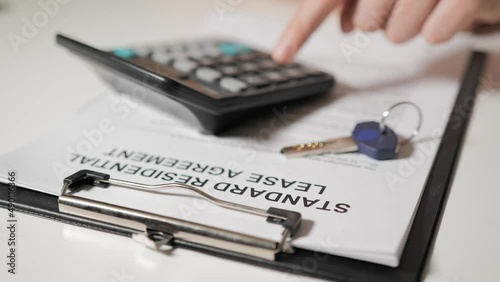 Standard tenancy agreement. The hands of realtor calculate the cost on calculator. In the foreground lies the key to the apartment or house.