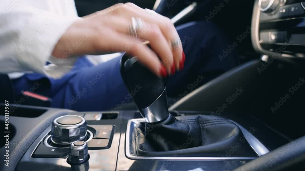 Business Woman controls auto and switch gears, turn on. A hand of driver girl is shifting the automatic gear in car close up. Female driving and changing gear on a beautiful sunny day.