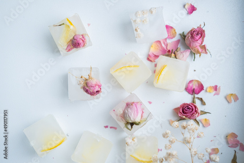 Ice cubes with flowers and lemon inside on a white background. Frozen flowers in ice. Edible flowers for decoration.