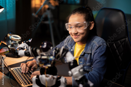 Portrait of girl sitting at desk in the evening, finishing soldering robot which is school project, child is watching tutorials, instructions on laptop, learning step by step how to fix electronics