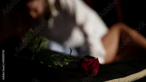lovers in bedroom in night, man and woman are having caress and sex in bed, red rose in foreground
