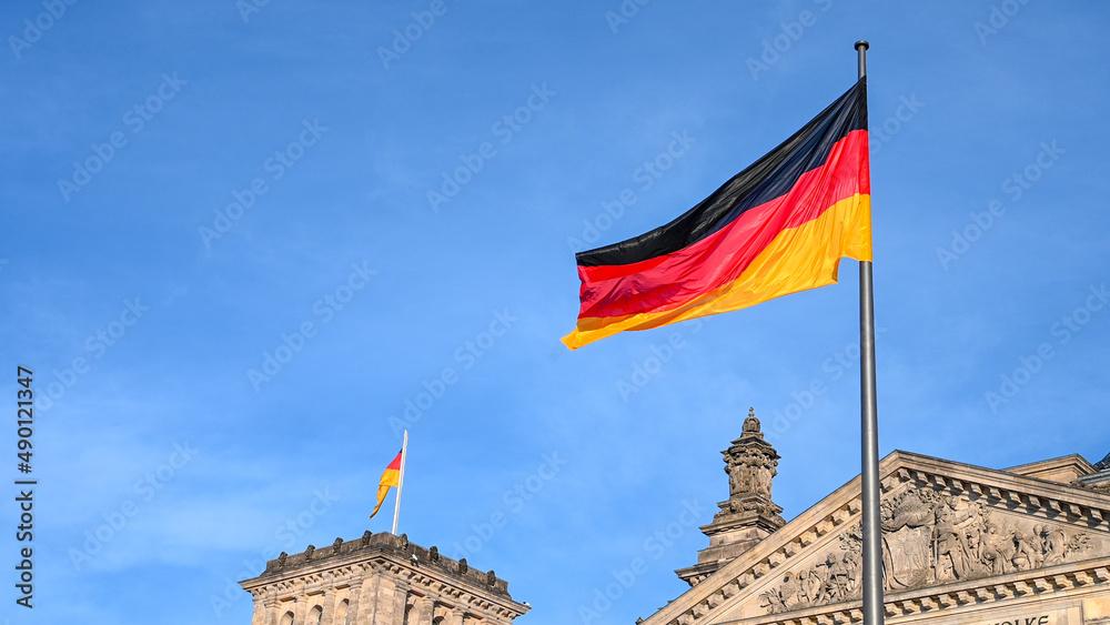 German flag flying on the wind. Waving flag of Germany on flagpole against blue sky. Deutschland. Black, red and yellow colors on German flag in a front of Bundestag in Berlin.