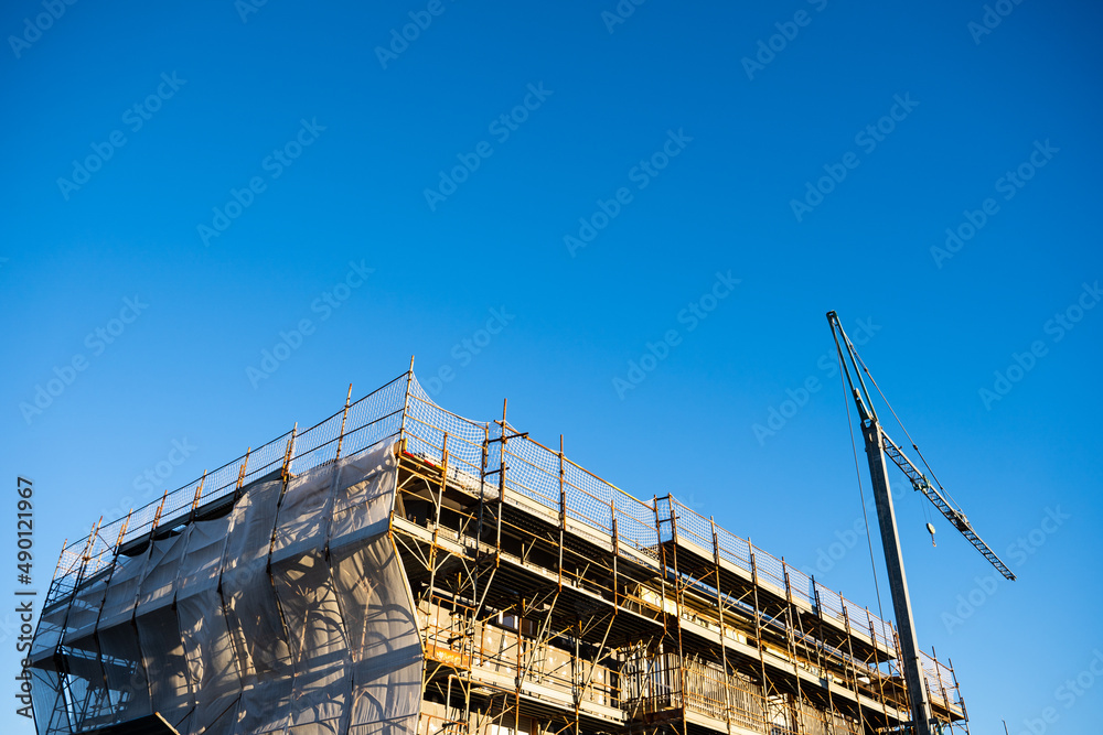 building under construction with scaffolding and cranes with sky background