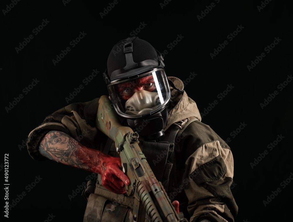 a man in a military uniform and a gas mask holds a weapon with bloody hands with an angry expression of emotions a man in a military uniform and a gas mask holds a weapon with bloody hands with an angry expression of emotions