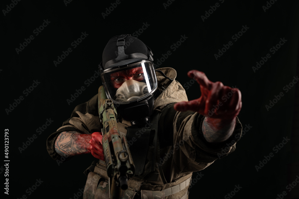 a man in a military uniform and a gas mask holds a weapon with bloody hands with an angry expression of emotions