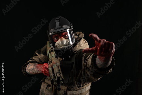 a man in a military uniform and a gas mask holds a weapon with bloody hands with an angry expression of emotions © rotozey