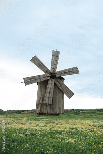 Old wooden windmill in a green field with chamomiles on clear sky background. Ecology concept