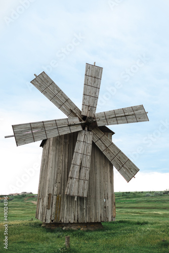 Old wooden windmill in a green field with chamomiles on clear sky background. Ecology concept