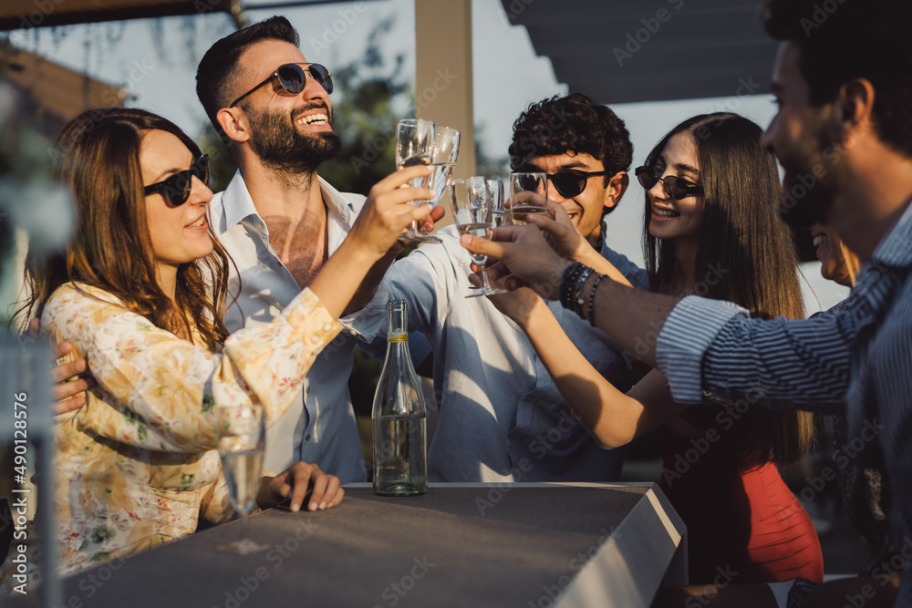 Young friends celebrating at sunset - toasting with flute glasses of white sparkling wine
