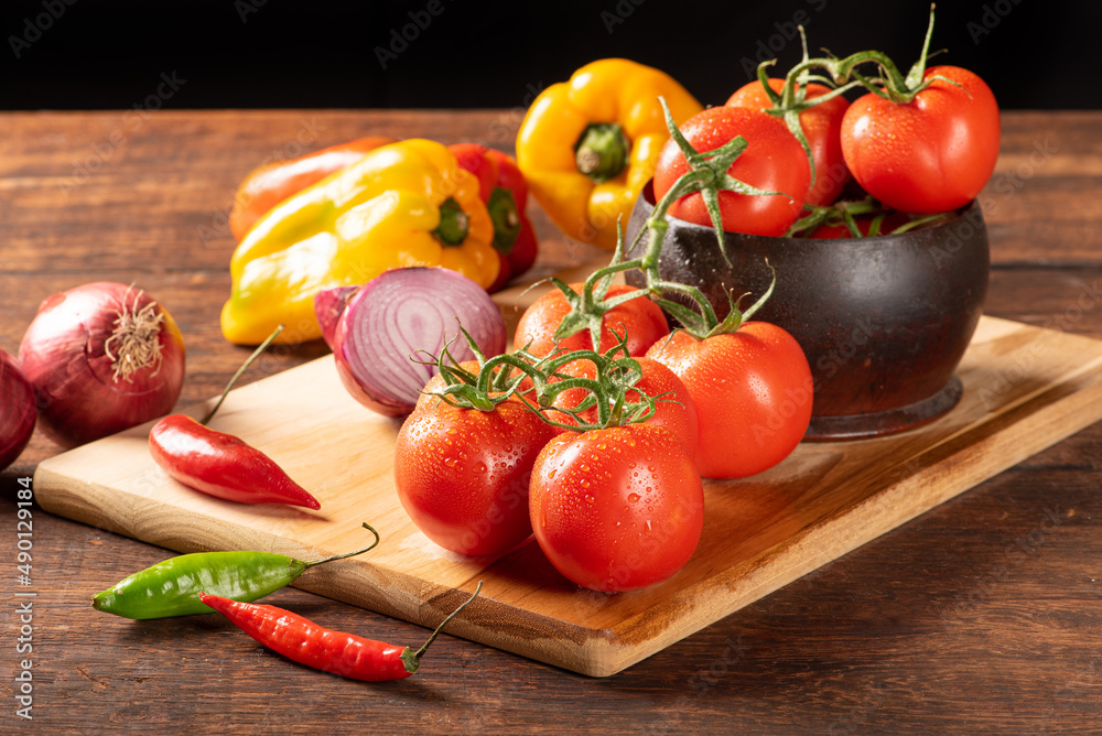 Table with red and yellow peppers, peppers, onions and garlic and tomatoes, over rustic wood, black background, selective focus. Table with red and yellow peppers, peppers, onions and garlic and tomatoes, over rustic wood, black background, selective focus.