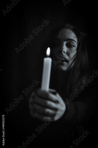 portrait of a young beautiful woman with very long hair who holds a lit candle in her hand and has a fixed and creepy gaze