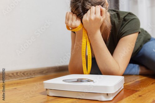 Fotografia White scale and depression, upset and sad woman with measuring tape on wooden fl