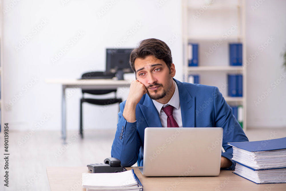 Young male employee unhappy with excessive work in the office Young male employee unhappy with excessive work in the office