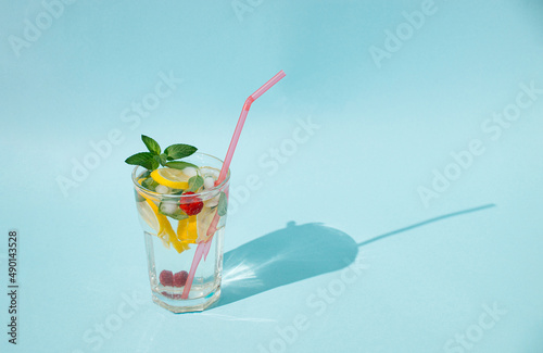 Glass of water with mint leaves, lemon slices, raspberries and ice cubes. Cold drink or refreshment concept. Minimal summer concept. Copy space.