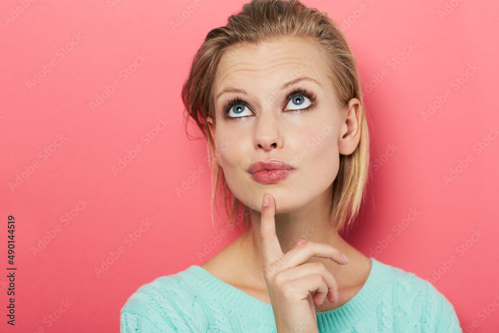 Fototapeta premium Hard choice. A beautiful young woman thinking to herself while isolated on pink.