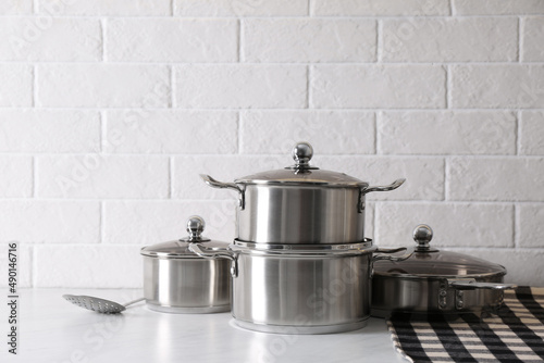 Set of stainless steel cookware on table near white brick wall