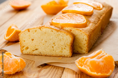 Loaf of delicious tangerine pound cake on parchment with pieces of mandarin on rustic wooden background. Delicious breakfast, traditional tea time treat. Reciepe of English orange pie loaf. photo