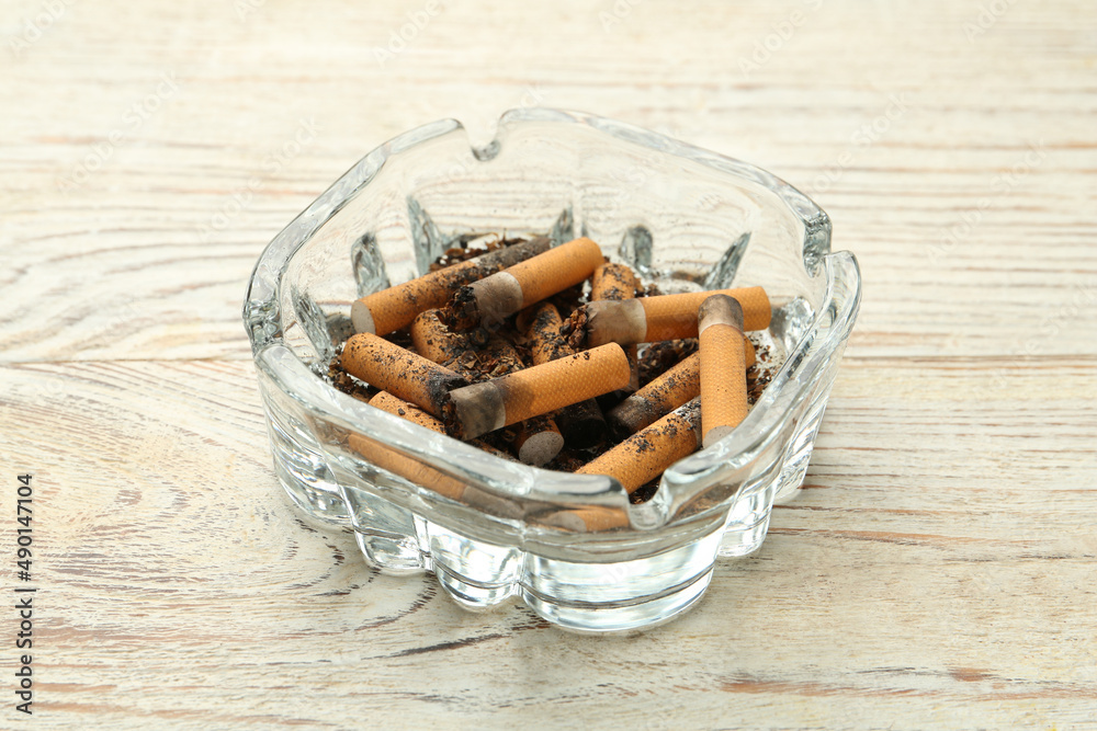 Glass ashtray with cigarette stubs on white wooden table Glass ashtray with cigarette stubs on white wooden table