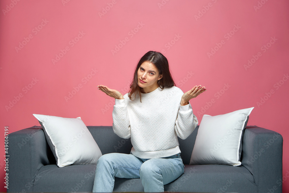 Puzzled young girl spreading hands, dont understand movie final, sitting on sofa. Dilemma, uncertainty concept Puzzled young girl spreading hands, dont understand movie final, sitting on sofa. Dilemma, uncertainty concept