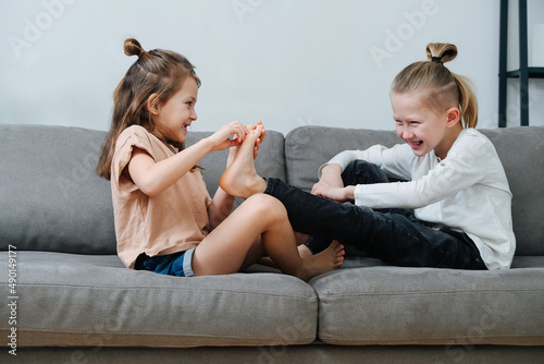 Billede på lærred Little girl trying to tickle boy's foot, they both laugh.