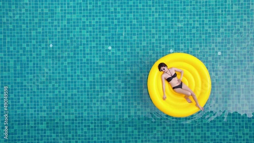 Beautiful young asian woman with yellow inflatable ring relaxing in swimming pool. top view
