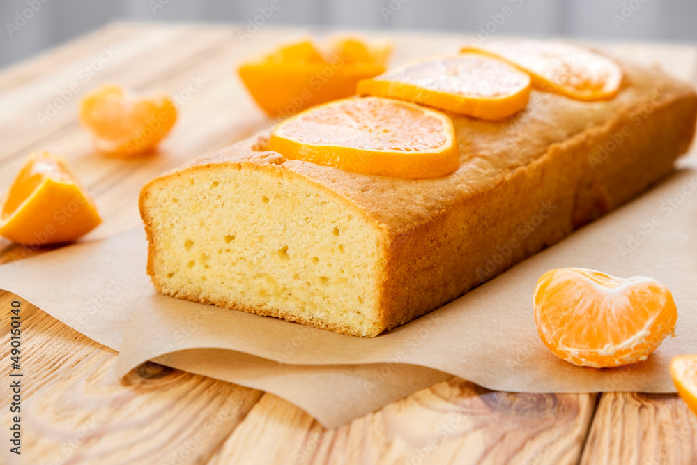 Moist mandarin pound cake on parchment with pieces of fresh tangerine on rustic wooden background. Delicious breakfast, traditional tea time treat. Reciepe of American lemon pie loaf. Moist mandarin pound cake on parchment with pieces of fresh tangerine on rustic wooden background. Delicious breakfast, traditional tea time treat. Reciepe of American lemon pie loaf.