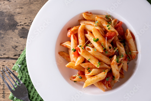 Pasta with tomato in red sauce on a white plate on wooden background. Top view.