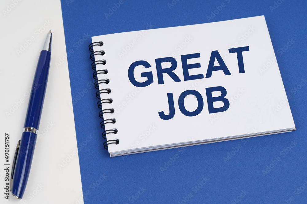 On a blue-white surface lies a pen and a notebook with the inscription - Great Job On a blue-white surface lies a pen and a notebook with the inscription - Great Job