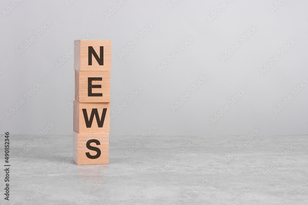 wooden cube on a concrete surface with text News. copy space on right for design, gray background