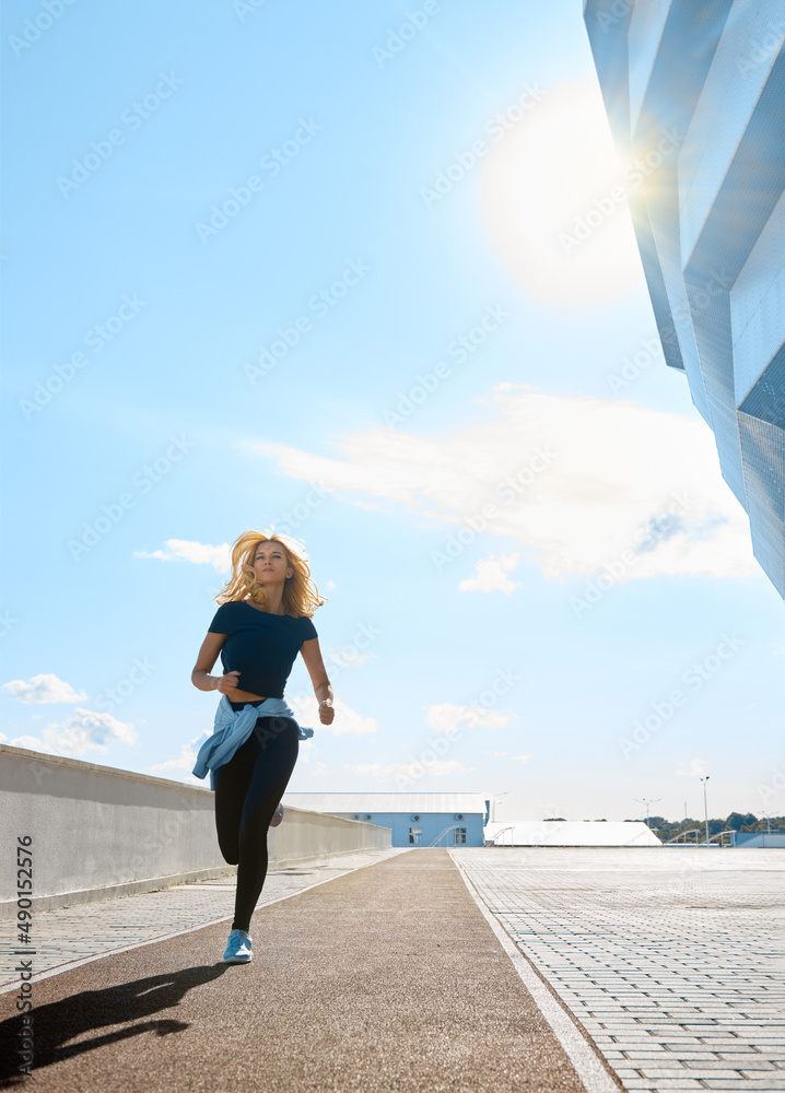 Young woman with fit body running on a sunny day. Female model in sportswear exercising outdoors. Female runner in black sportive clothes doing fitness