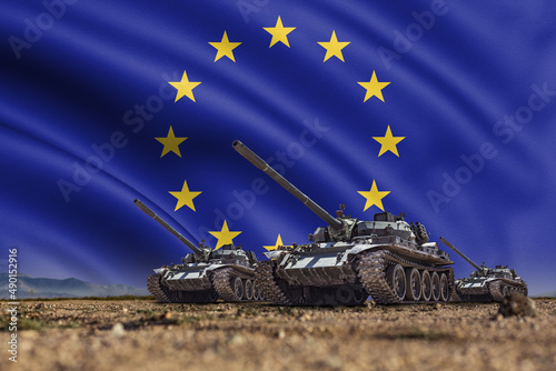 Tanks lined up in front of a European Union or EU flag. Several military army war battle tank vehicles on the terrain ready to attack