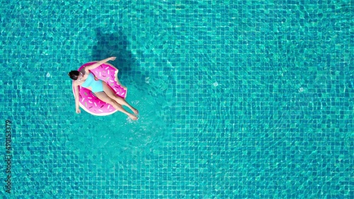 Top view of young asian woman in swimsuit on the pink donut lilo in the swimming pool.