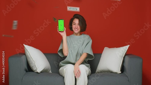 Lucky young girl use phone with green mock-up screen win money, sitting on sofa. Financial success, jackpot