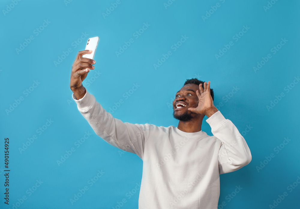 Portrait of an African-American man taking a selfie and smiling on a blue isolated background Portrait of an African-American man taking a selfie and smiling on a blue isolated background