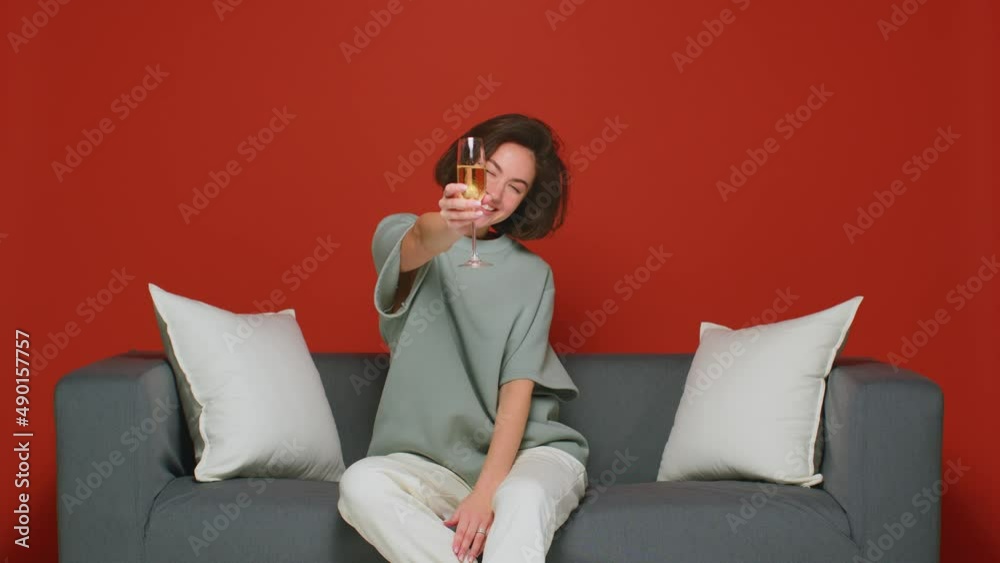 Modern young girl holding glass with champagne, clink, celebrating holiday, sitting on sofa on party, feels happy Modern young girl holding glass with champagne, clink, celebrating holiday, sitting on sofa on party, feels happy