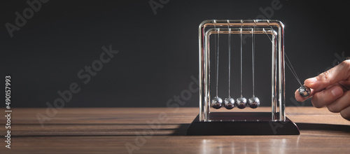 Male hand showing Newton's cradle balls on the wooden table. Business photo
