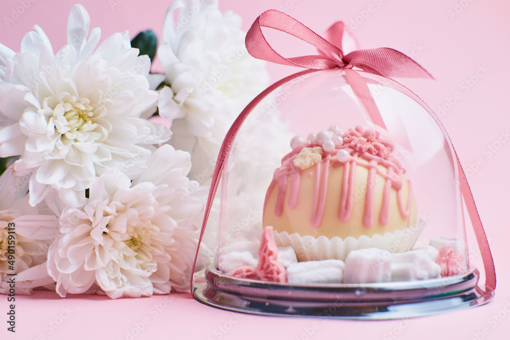 Chocolate candy in a gift box on a pink background with flowers