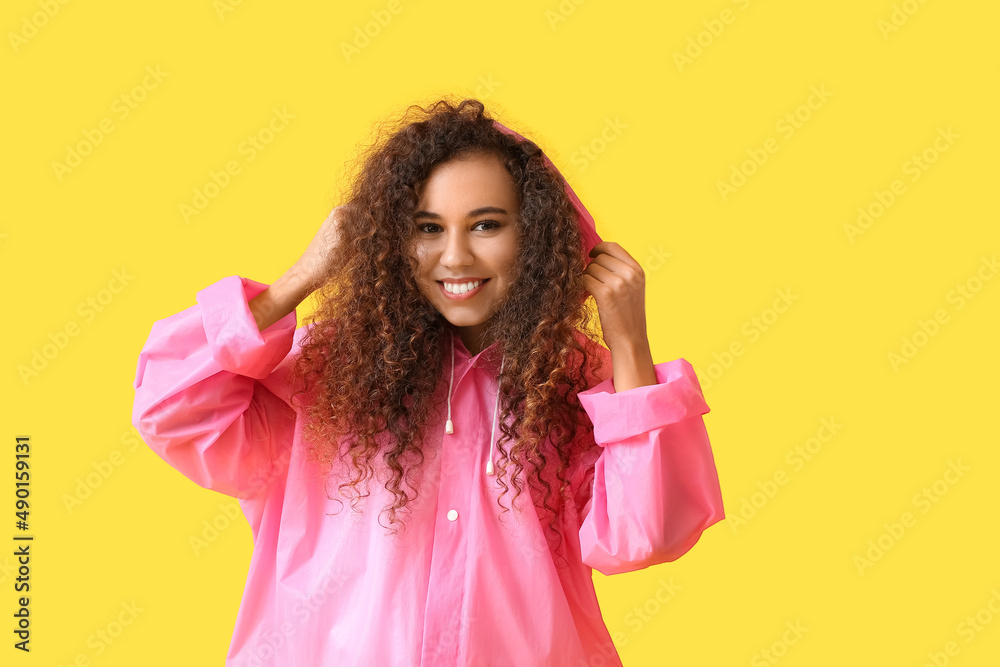 Smiling young African-American woman in pink raincoat on yellow background