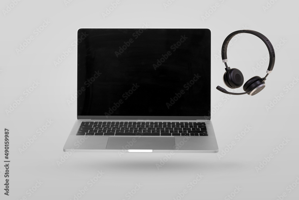 Laptop computer with empty screen and headset levitating in the air on a gray background. Creative minimal background. Laptop computer with empty screen and headset levitating in the air on a gray background. Creative minimal background.