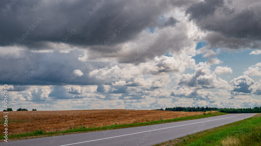 The rural road goes over the horizon. Storm clouds over the field. The rural road goes over the horizon. Storm clouds over the field.