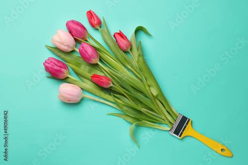 Brush with colorful tulips on turquoise background  top view. Creative concept