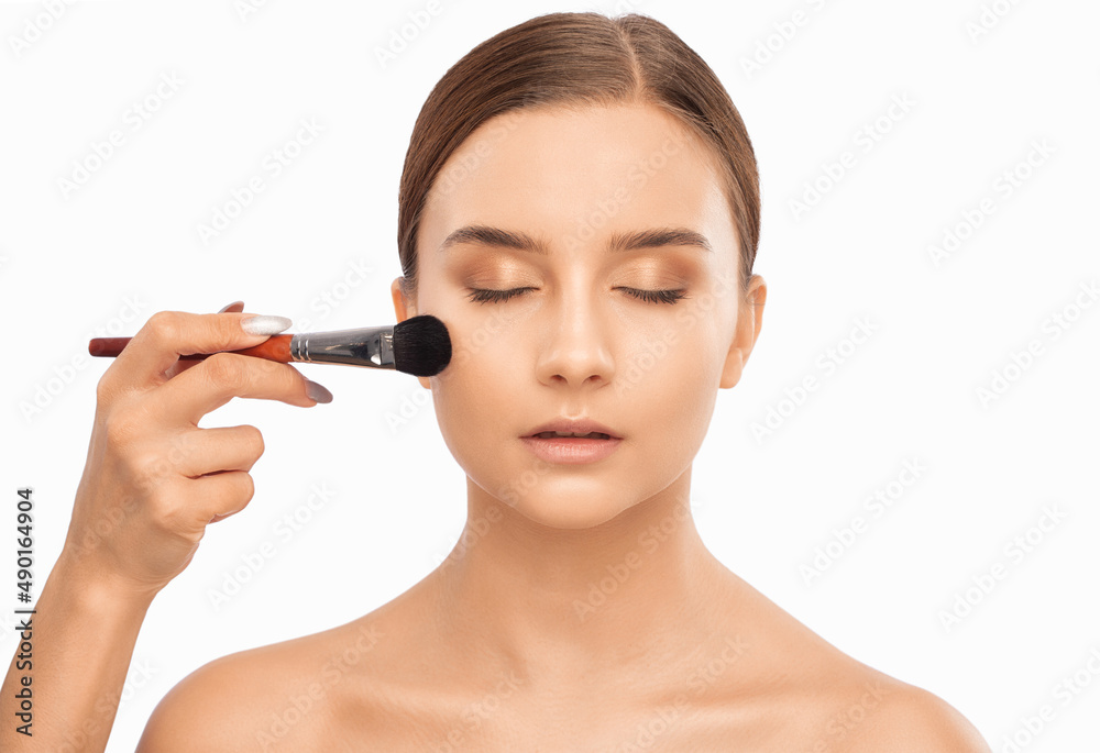 Portrait of a beautiful brunette girl with beautiful fresh makeup and healthy clean skin.Makeup artist holds a powder brush in her hands. Professional makeup concept