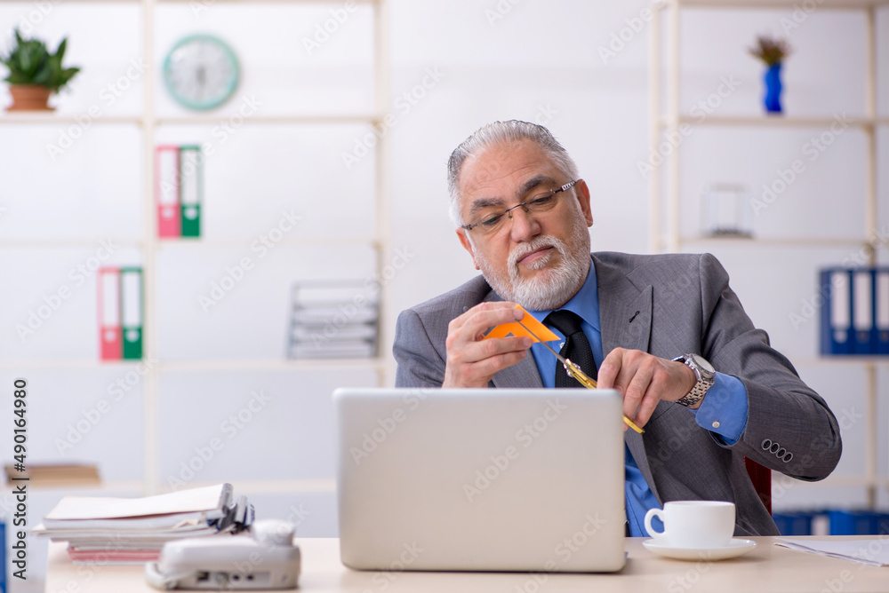 Old male employee holding scissors in the office Old male employee holding scissors in the office