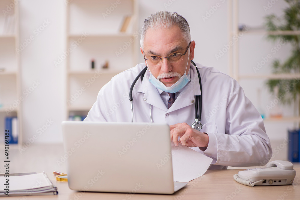 Old male doctor working in the clinic during pandemic Old male doctor working in the clinic during pandemic